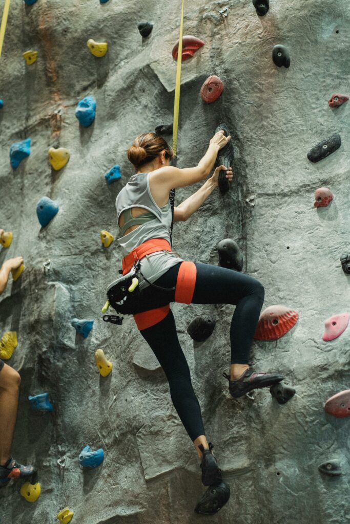 Full body of woman in sportswear training on climbing wall during workout in gym